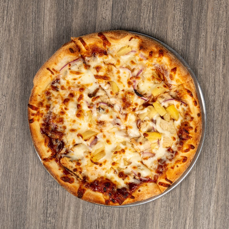 Cheesy Hawaiian-style pizza topped with pineapple, chicken, red onion, and barbecue sauce on a metal tray.