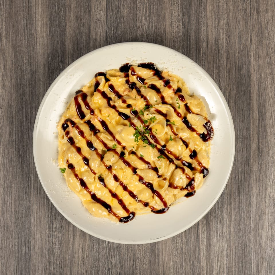 Creamy shell pasta topped with dark balsamic drizzle, grated cheese, and chopped parsley on a white plate.