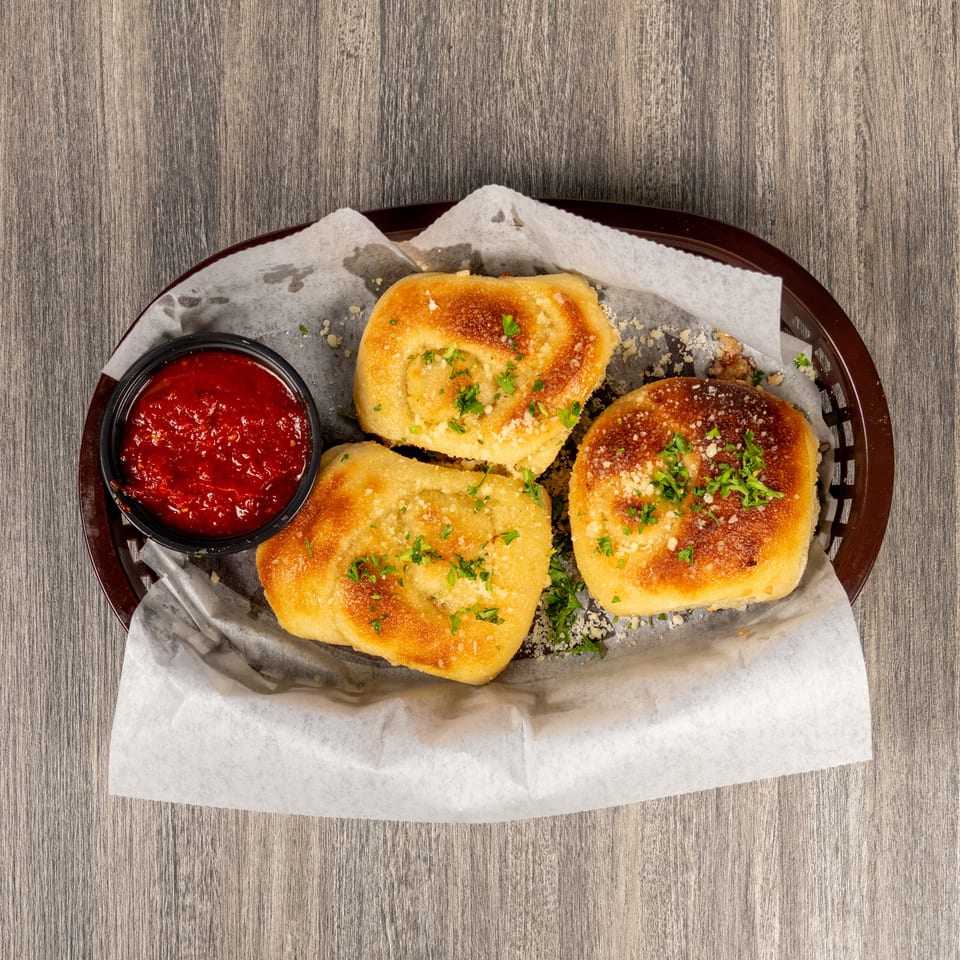 Three golden garlic bread rolls topped with parsley and Parmesan, served with marinara sauce in a lined basket.