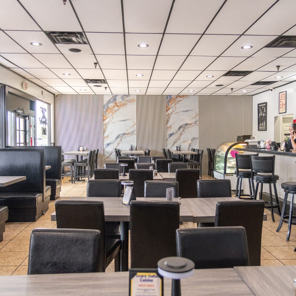 Bright modern restaurant dining room with black leather booths, tables, marble wall panels, and a counter with display case.
