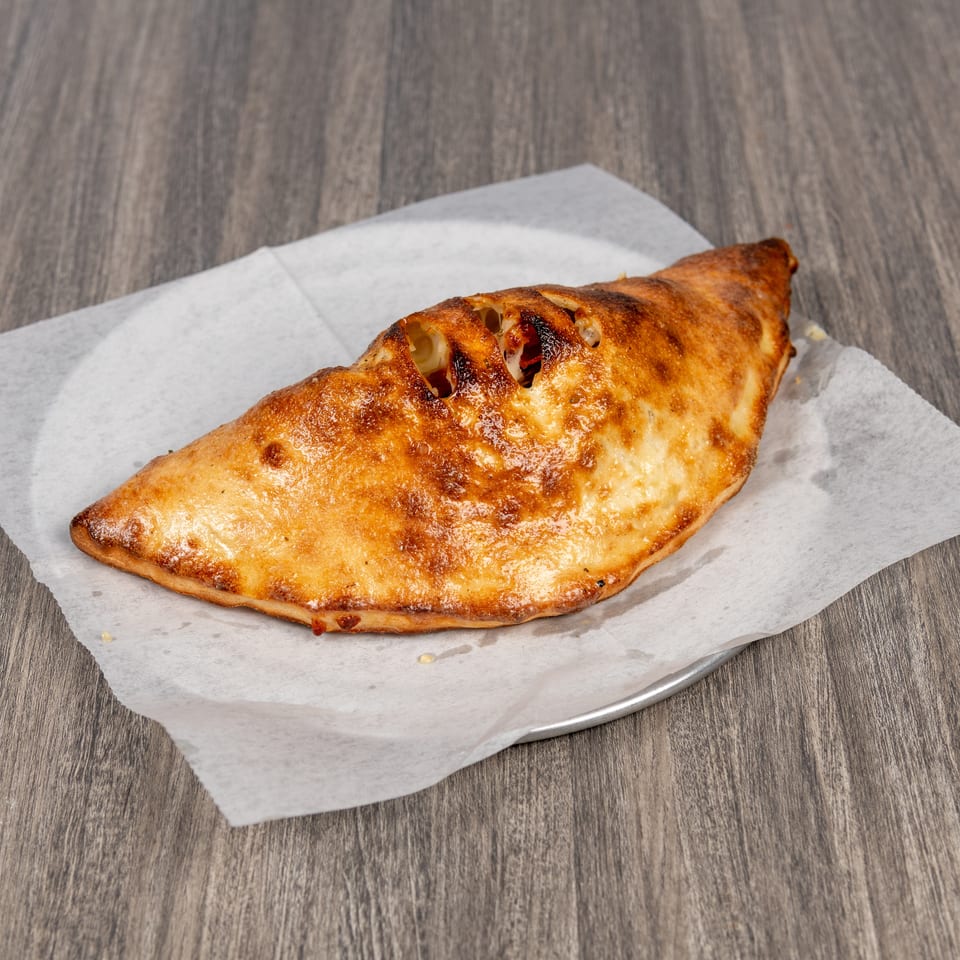 Golden-brown baked calzone with melted cheese visible through slits, resting on parchment paper atop a wooden table.