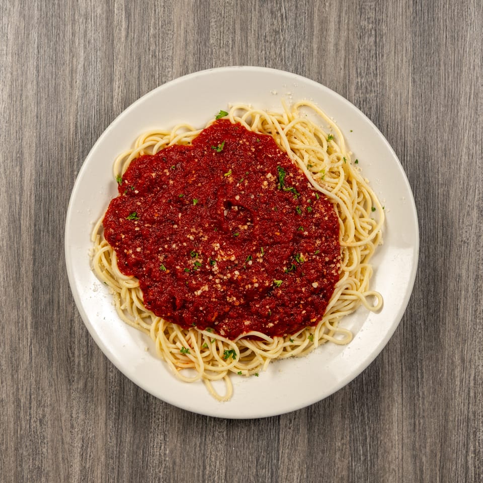 Plate of spaghetti topped with red tomato sauce, grated cheese, and parsley on a wooden table.