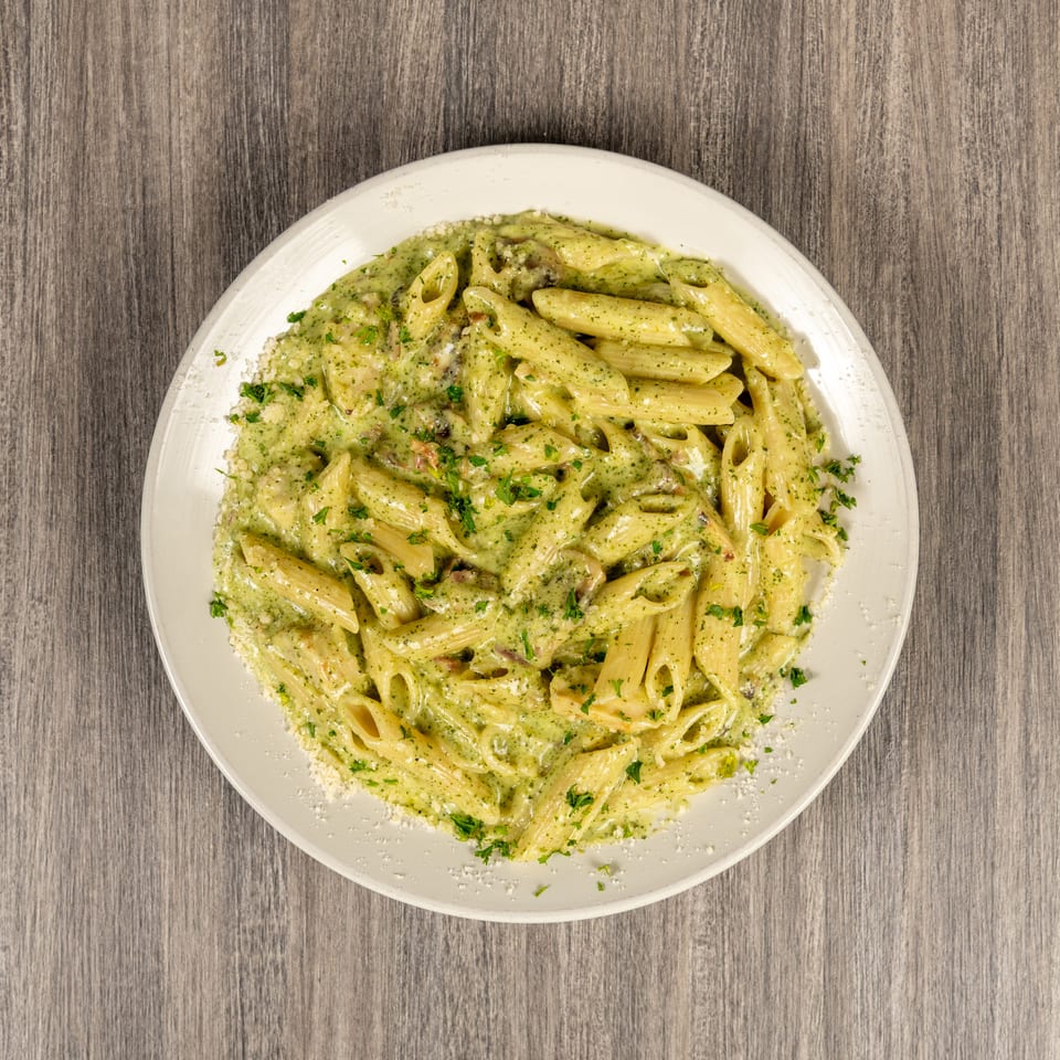 Overhead view of penne pasta in creamy green herb sauce, garnished with parsley and grated cheese on a white plate.