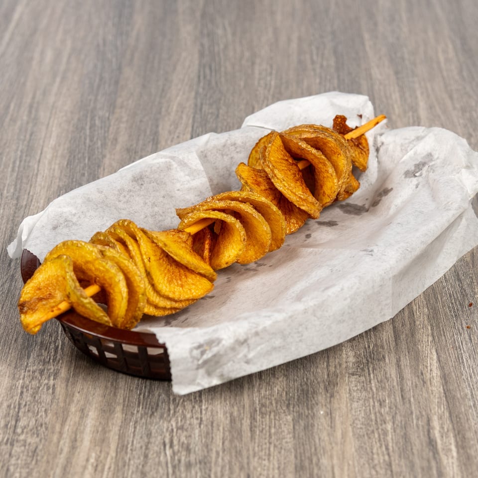 Golden spiral-cut potato skewer served in a paper-lined basket on a wooden table.