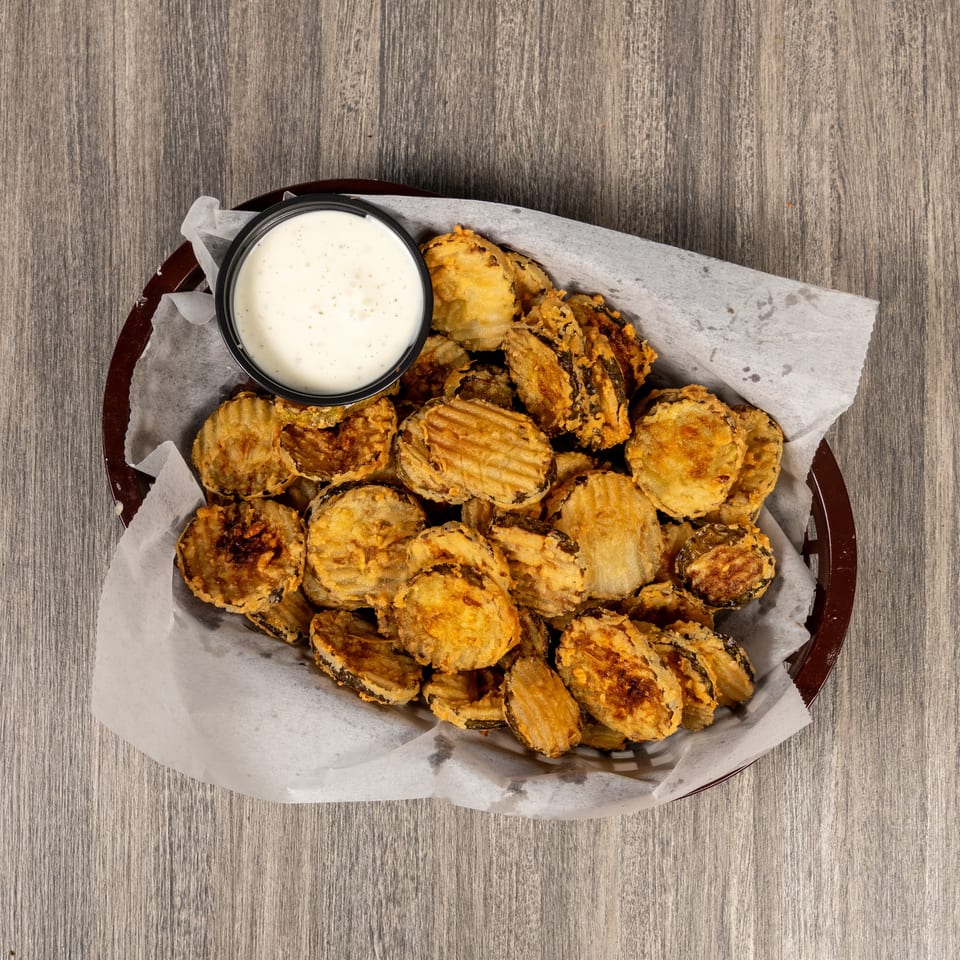 Basket of golden fried vegetable slices served with creamy dipping sauce on parchment paper over a wooden table.