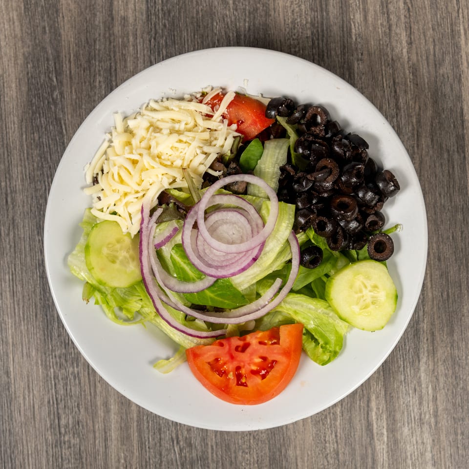 Garden salad with lettuce, shredded cheese, black olives, tomatoes, cucumbers, and red onion on a white plate.