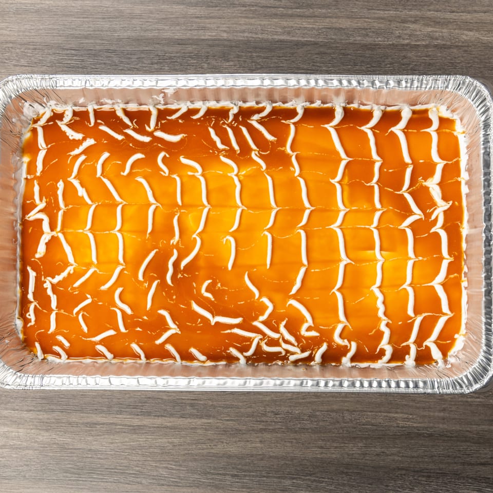 Large aluminum tray of orange-glazed dessert decorated with white icing in a geometric pattern on a wooden table.