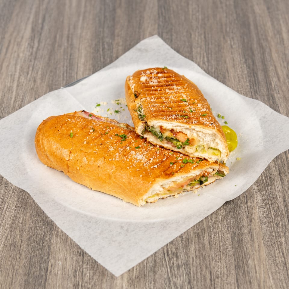 Grilled panini sandwiches with toasted bread, vegetables, and meat, sprinkled with herbs and crumbs on parchment paper.