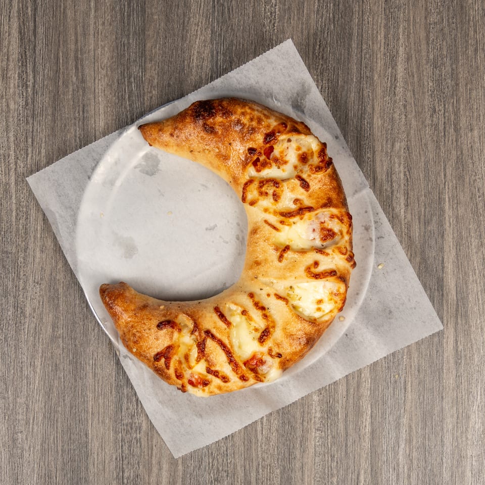 Golden-brown, cheese-covered calzone arranged in a ring on parchment paper over a wooden table.