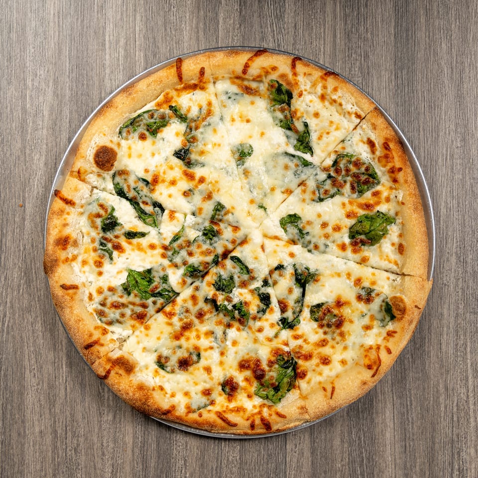 Overhead view of a golden-crusted pizza topped with melted cheese and leafy greens on a metal tray.